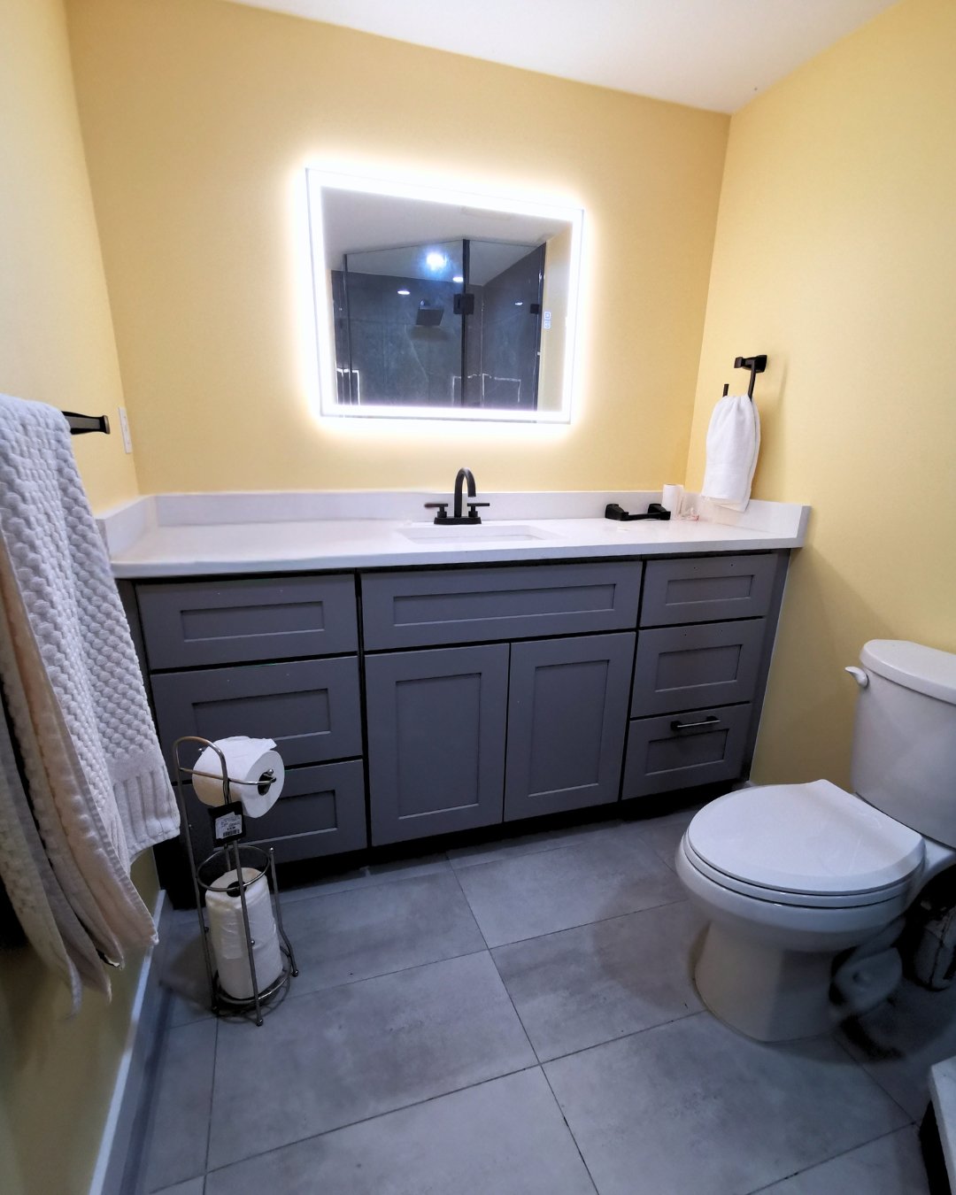 Condo Renovation in Coquitlam: Spacious bathroom with white countertops, silver fittings, and dark double-door storage.