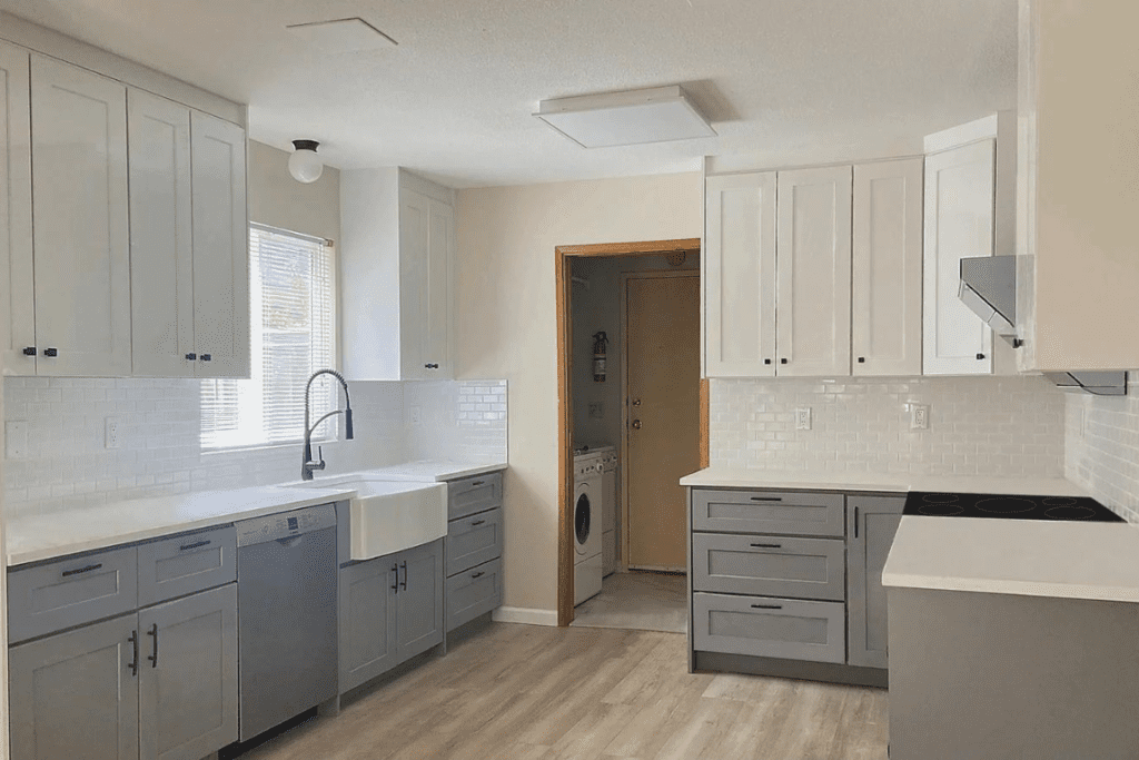 Modern two-tone kitchen with white upper cabinets, gray lower cabinets, farmhouse sink, white subway tile backsplash, and light wood flooring.