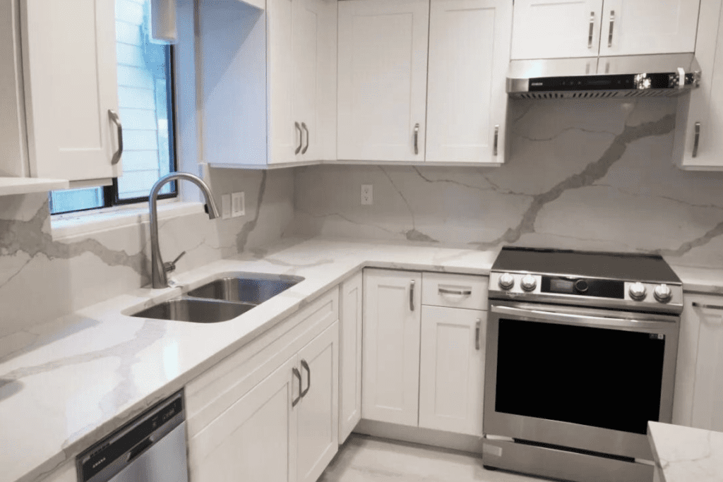After Home Renovation in Richmond: Sleek kitchen with white cabinetry, marble countertops, and stainless steel appliances.
