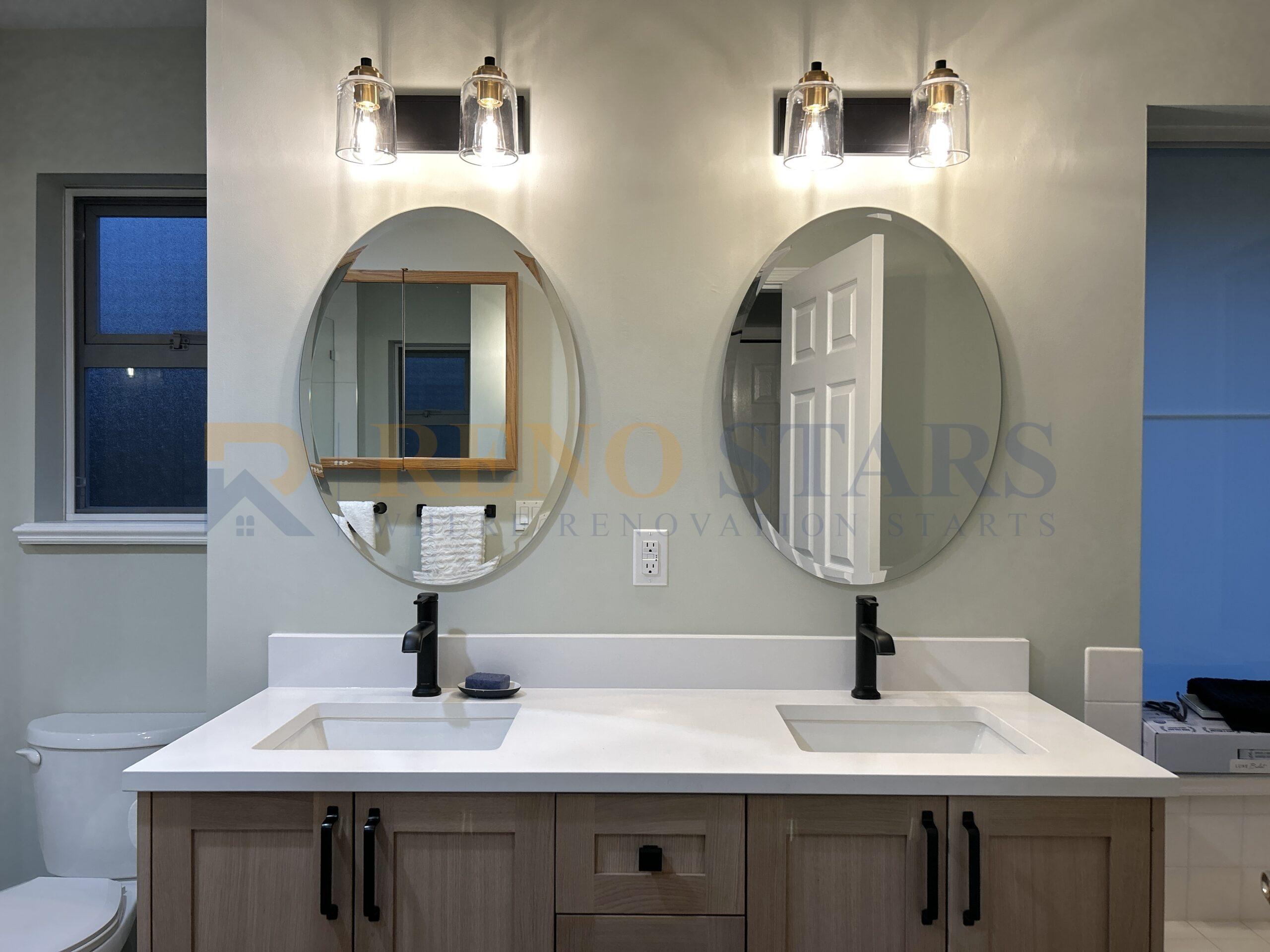 Double vanity with oval mirrors and wall-mounted lighting.