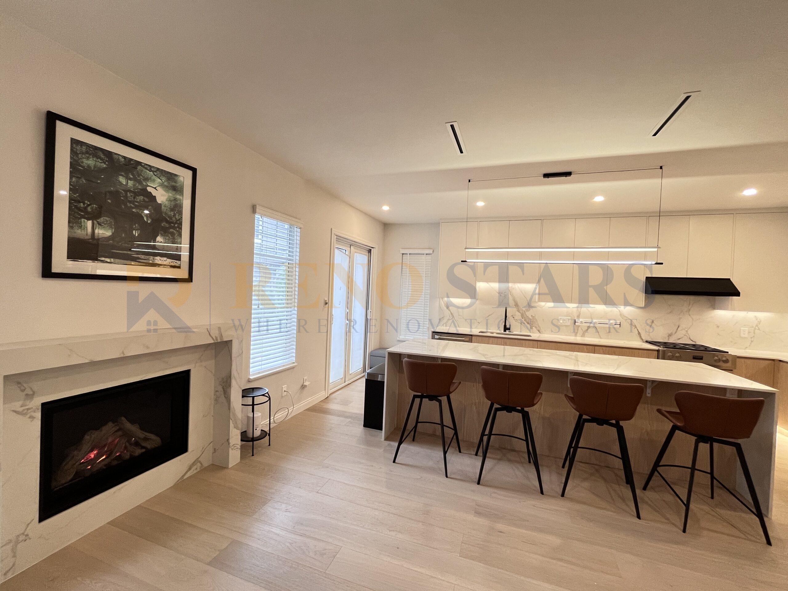 Modern open kitchen with marble island, fireplace, and bar seating.