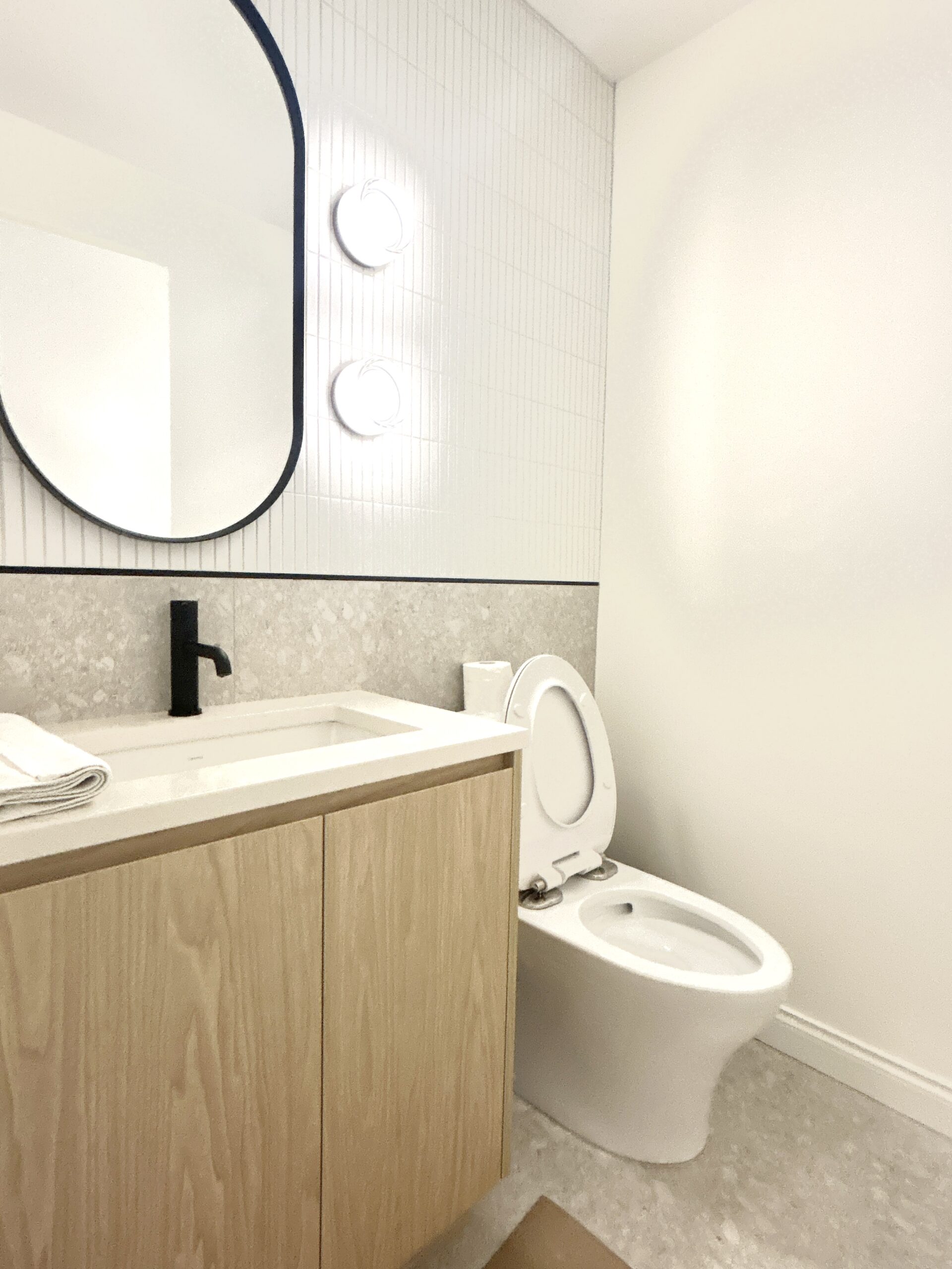 Minimalist bathroom with wood vanity, white countertop, and black fixtures.