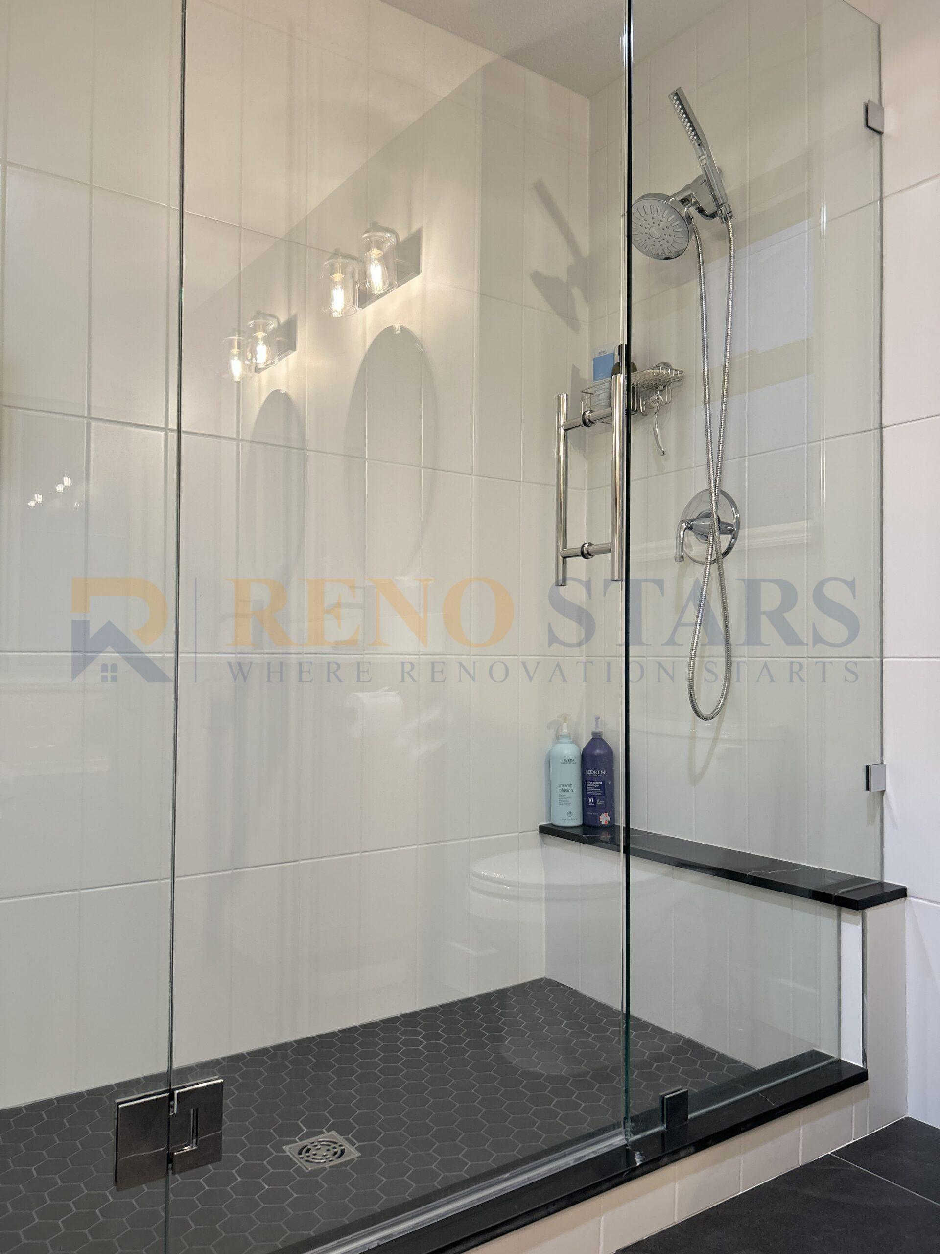 Glass-enclosed shower with dual showerheads and black bench.