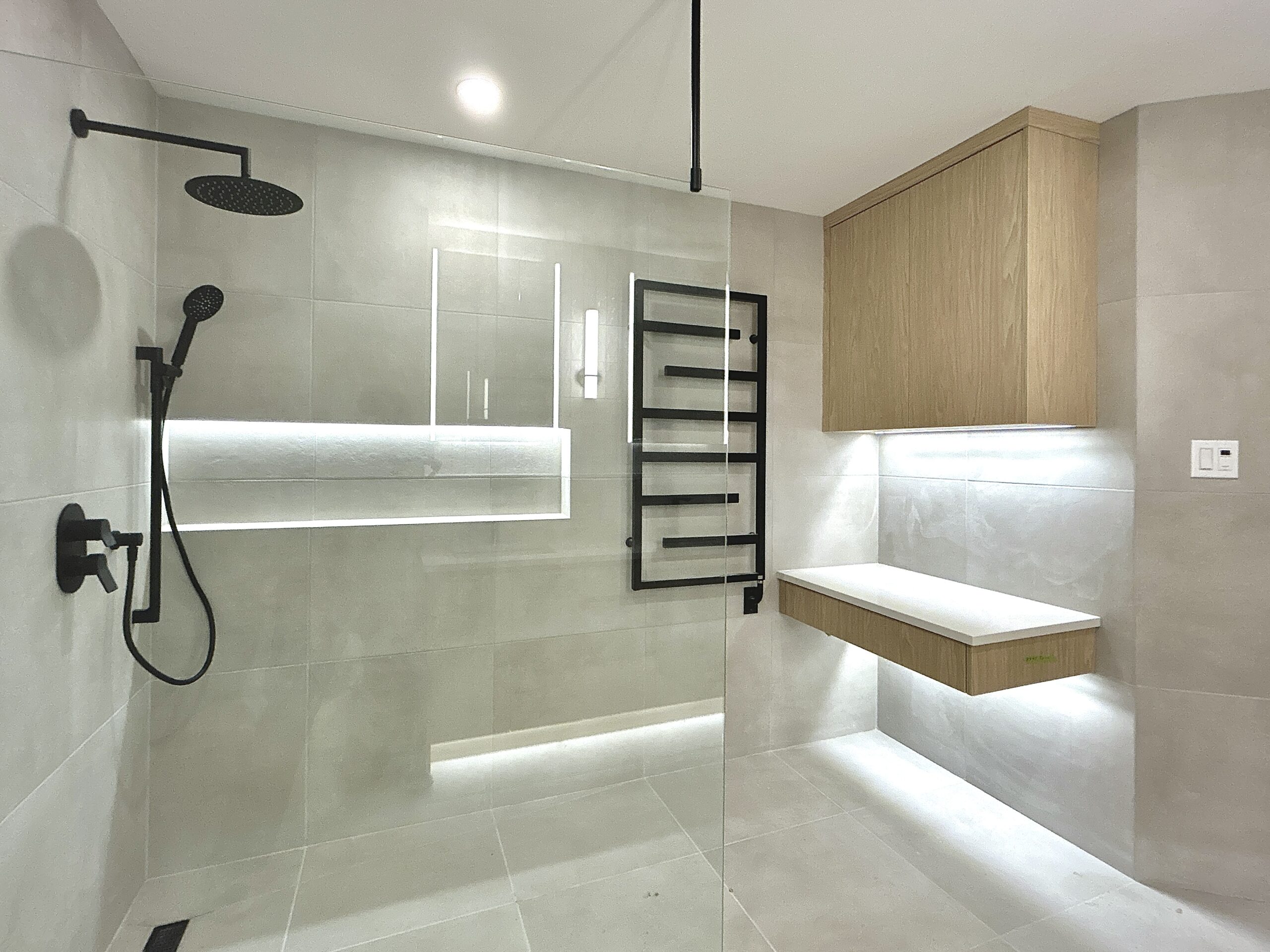Minimalist walk-in shower with black fixtures, wood cabinets, and LED lighting.
