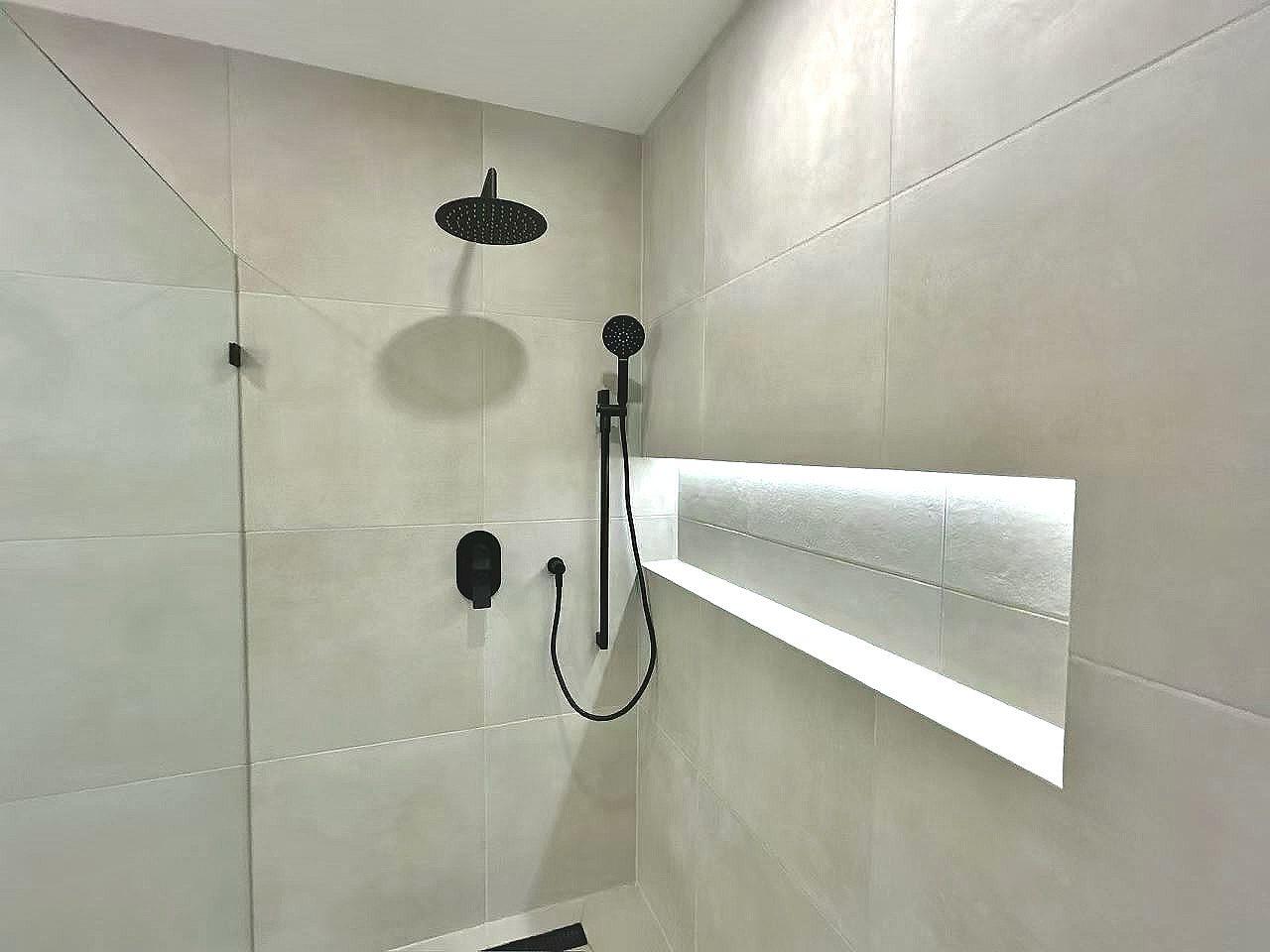 Minimalist walk-in shower with black rain shower head and built-in wall niche.